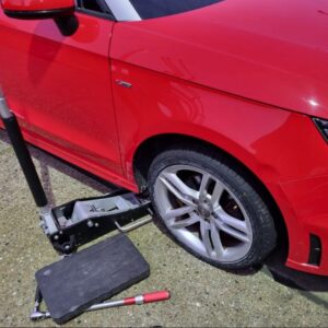 Red car lifted with jack for tyre fitting service